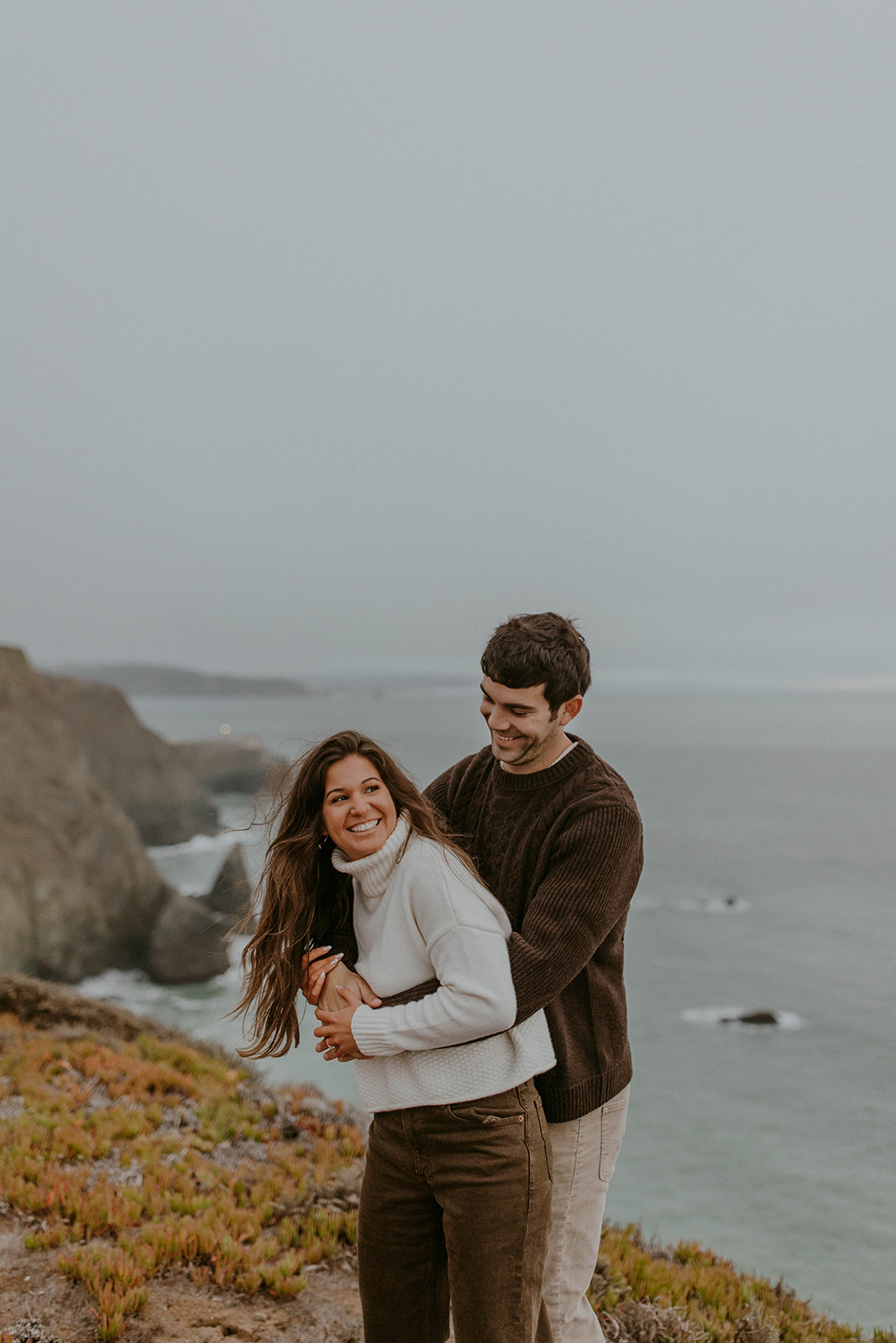 a couple in a playful pose on the california coast during winter engagement photo session. Photo taken by Codi Baer Photography 