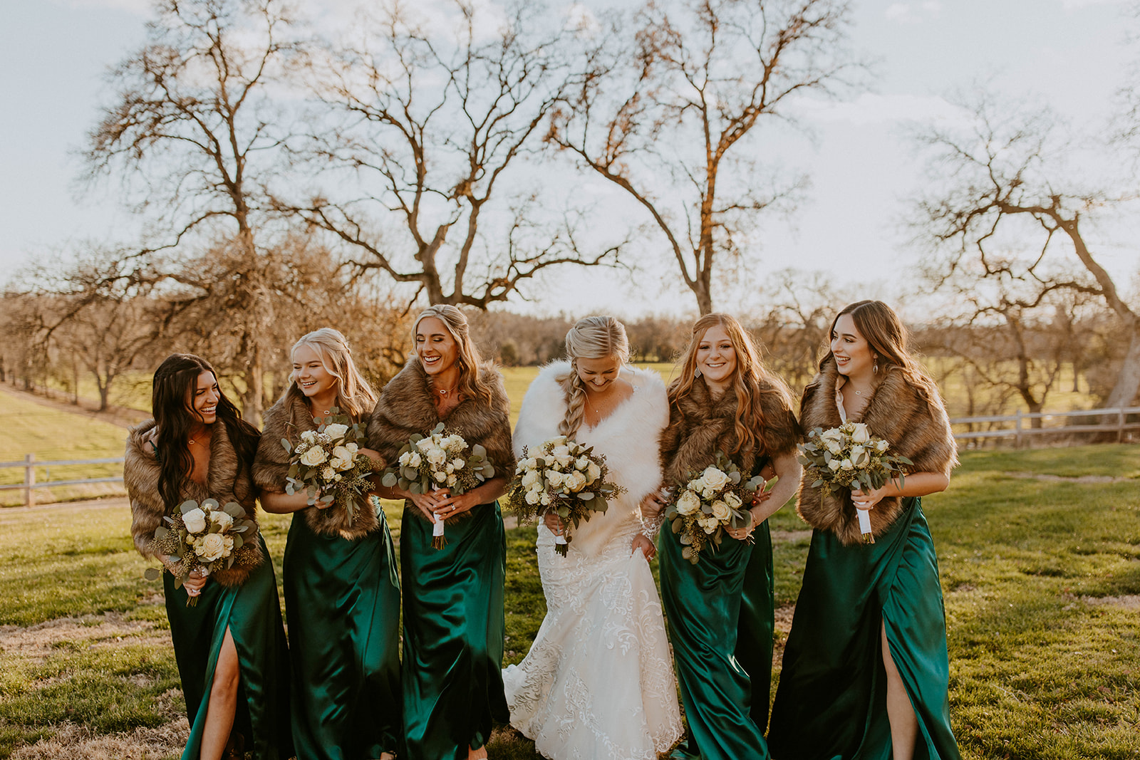 bridesmaids wear satin forest green bridesmaid dresses for this winter wedding. the bride and her bridesmaids walk towards the camera and laugh together. photo by codi baer photography