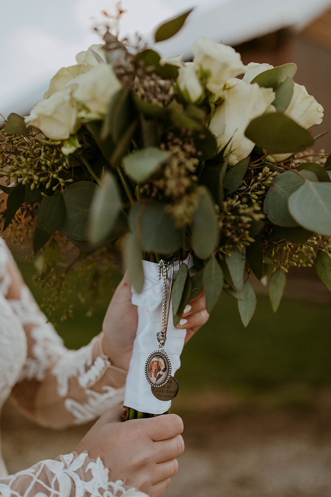 a bride holds her bouquet that has a portrait of her parents on their wedding day in a small locket tied around her wedding flowers. photo taken by codi baer photography
