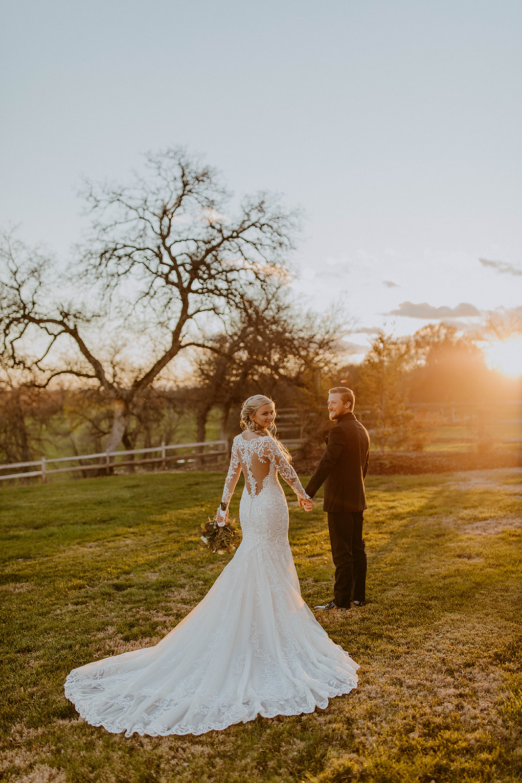 bride and groom pose for photos at sunset during their wedding. the bride wears an open back long sleeve lace wedding dress. photo taken by codi baer photography
