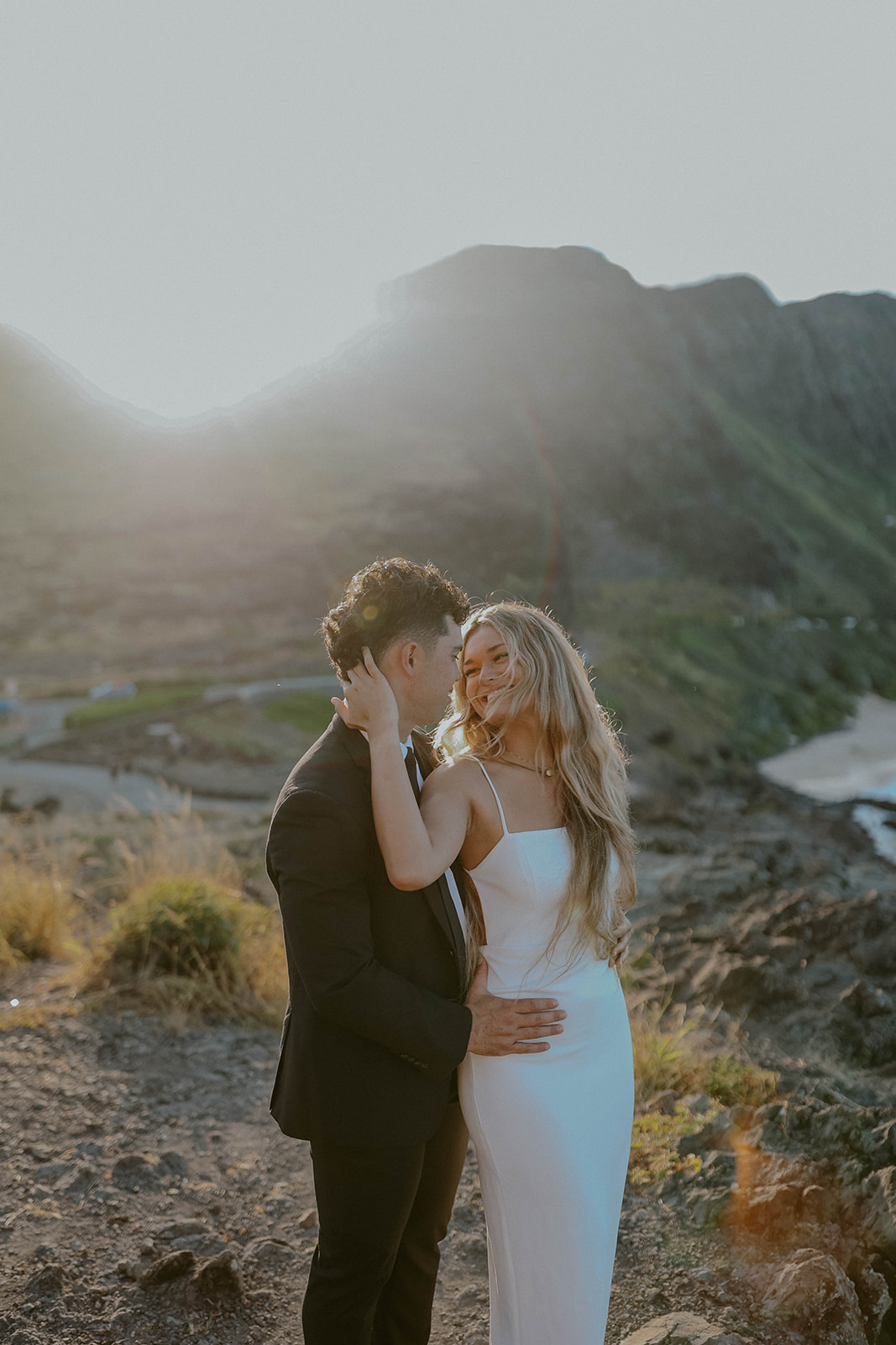 a bride and groom look at one another while posing on a cliff during their oahu elopement at sunset
