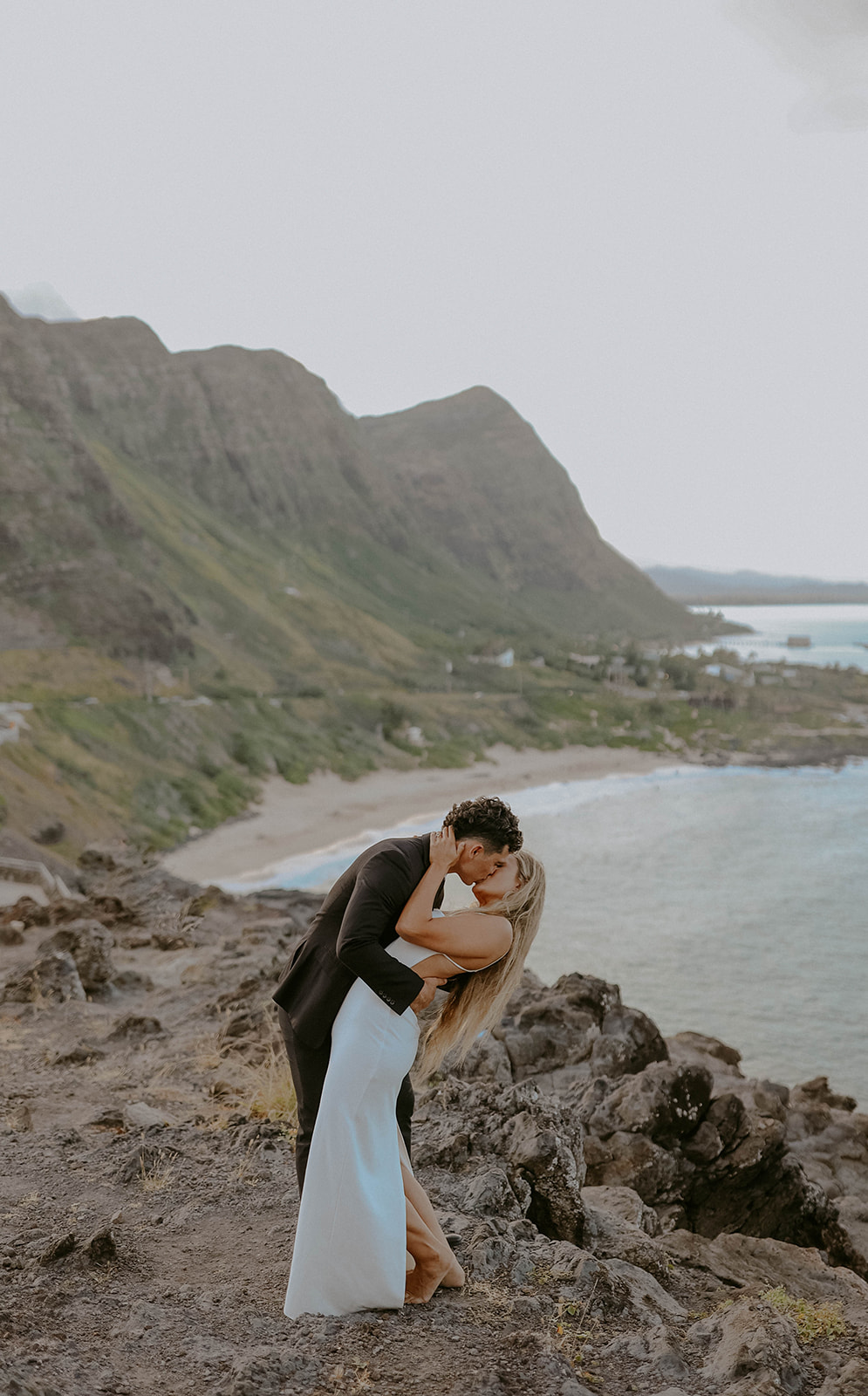 a groom kisses his bride at their elopement ceremony on a cliff overlooking the pacific ocean in oahu hawaii