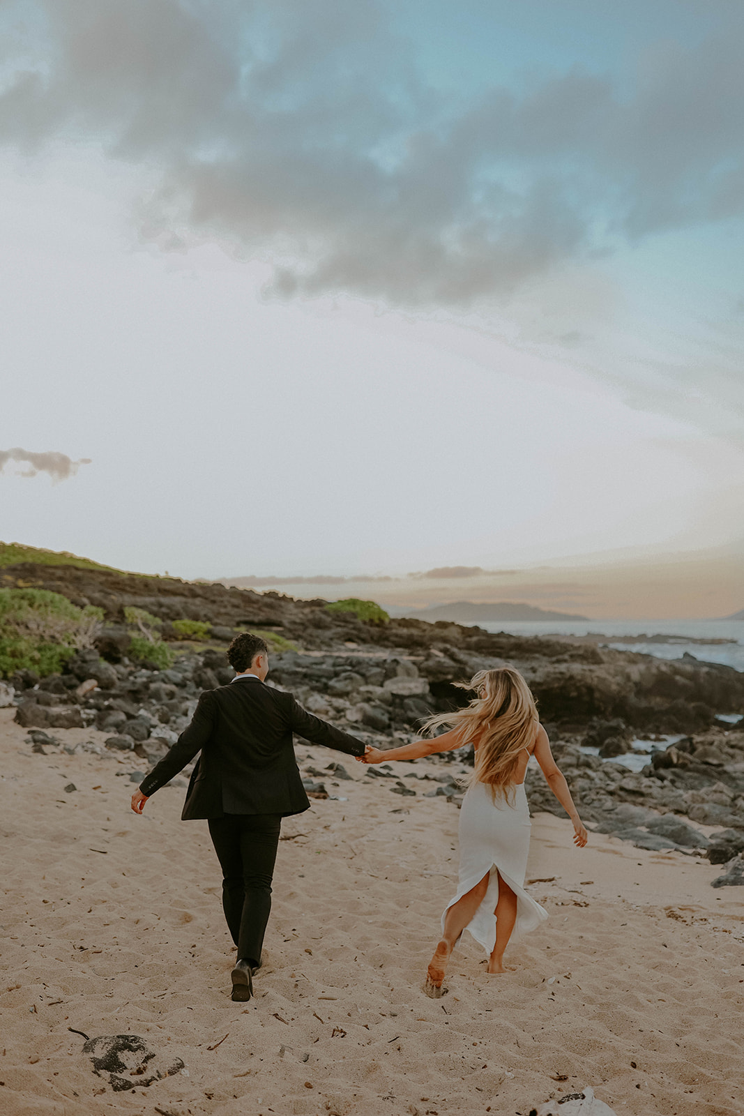 a couple runs on the beach holding hands during their oahu elopement in hawaii
