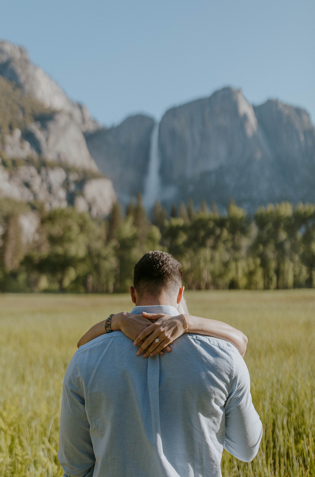 woman hugs her fiance during yosemite engagement photoshoot with waterfall in background
